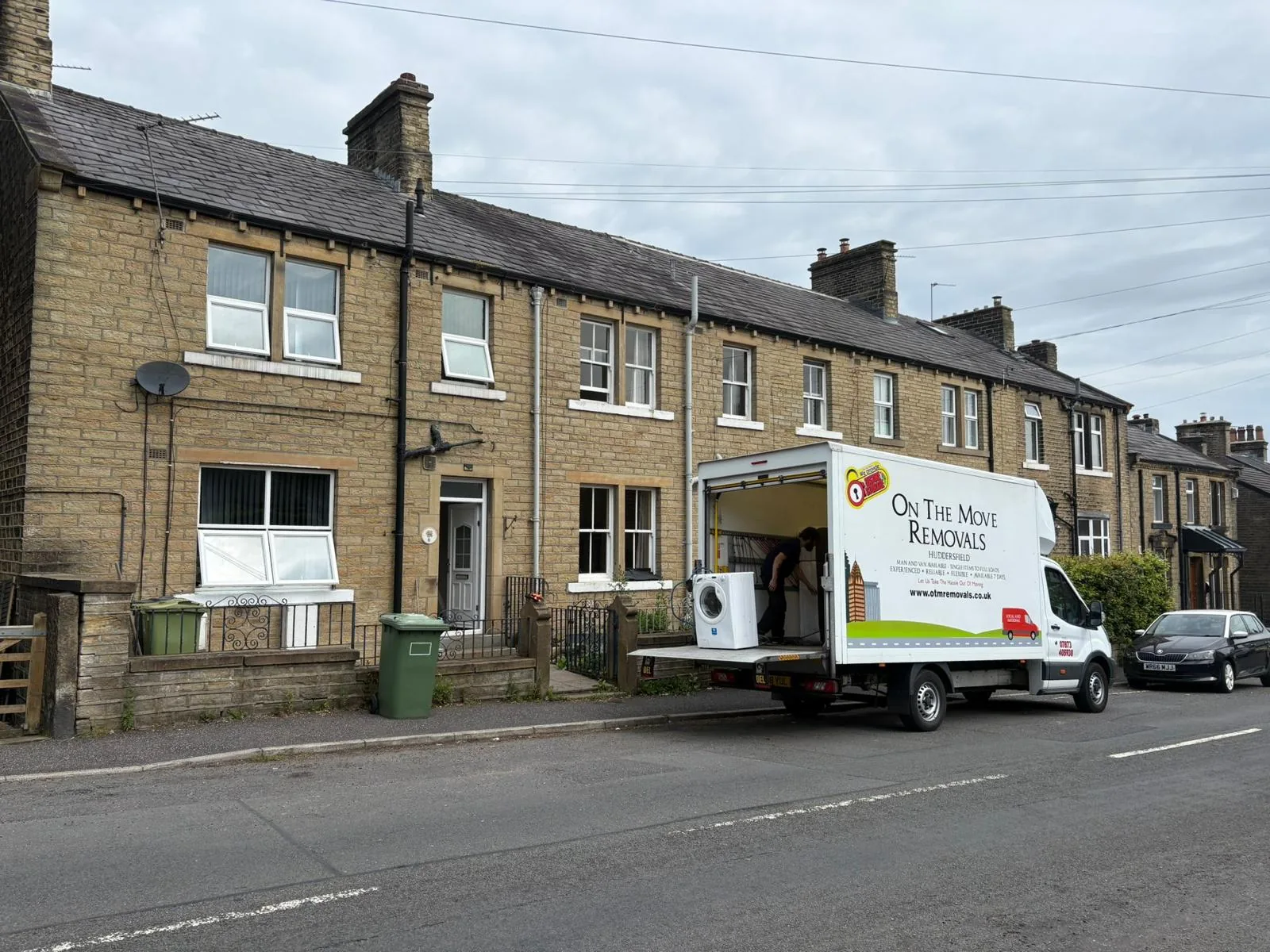 Branded removal van loading a washing machine outside stone terraced houses by On The Move Removals in Leeds