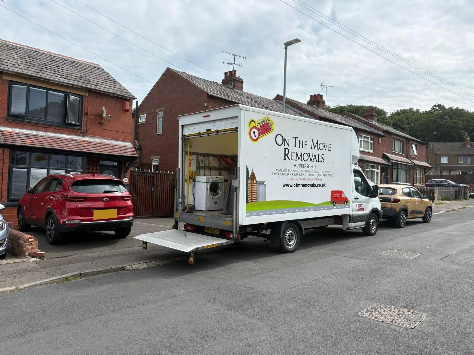 Branded removal van with a washing machine outside a brick residential street by On The Move Removals in Brighouse