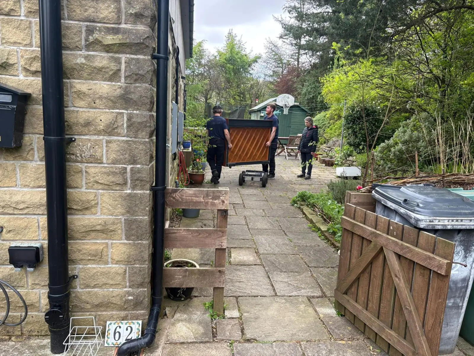 On The Move Removals two-person team carrying a wrapped upright piano along a stone passageway during a specialist piano move in Marsden