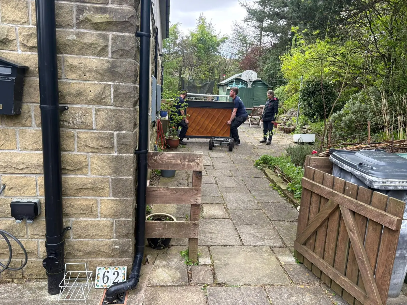 On The Move Removals team manoeuvring a wrapped upright piano through a narrow stone passageway during a Marsden piano removal