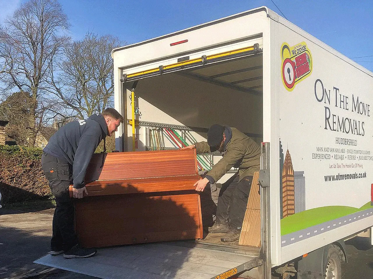 On The Move Removals two-person team unloading a wrapped upright piano off the back of a branded OTM van during a Huddersfield piano removal