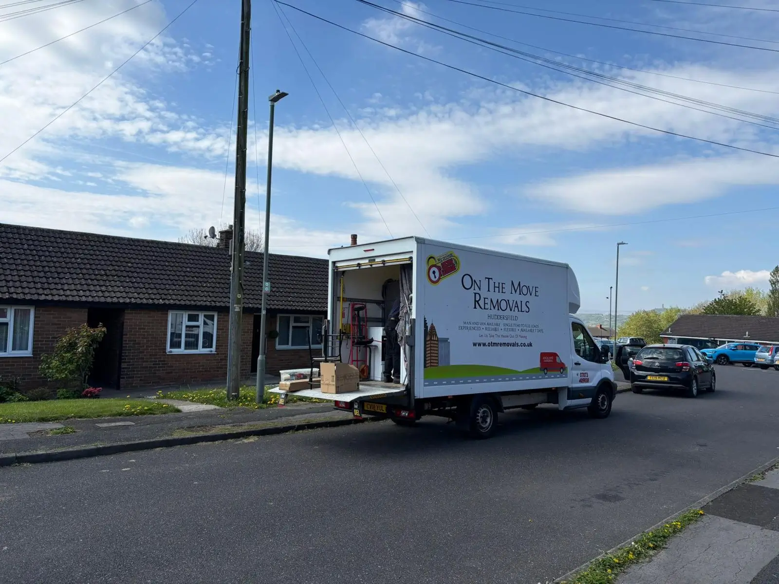 On The Move Removals van with ramp down loading belongings at a residential bungalow in Oakes, Huddersfield