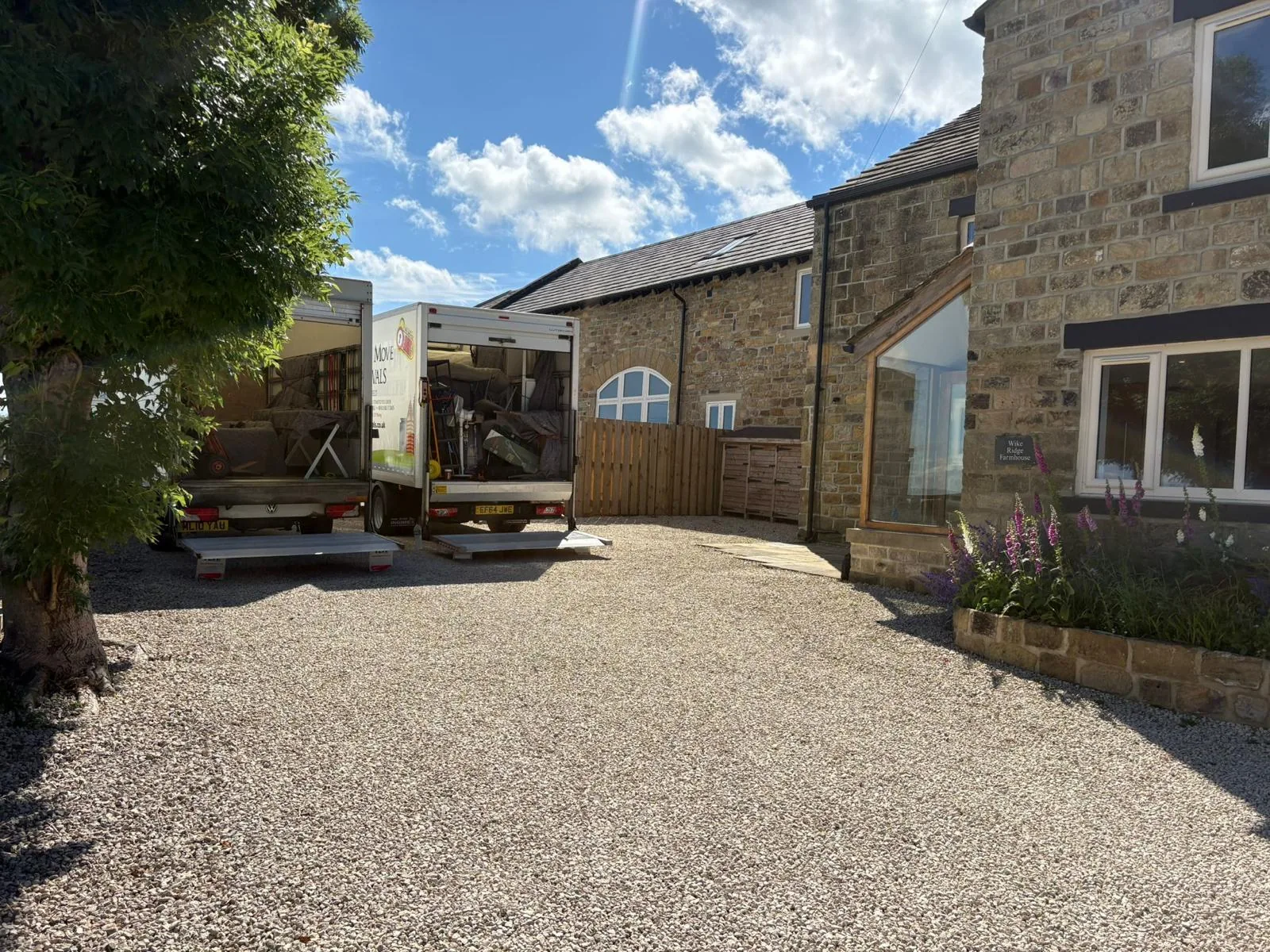 Two branded removal vans partly loaded outside a stone farmhouse on a gravel drive by On The Move Removals in Meltham Huddersfield